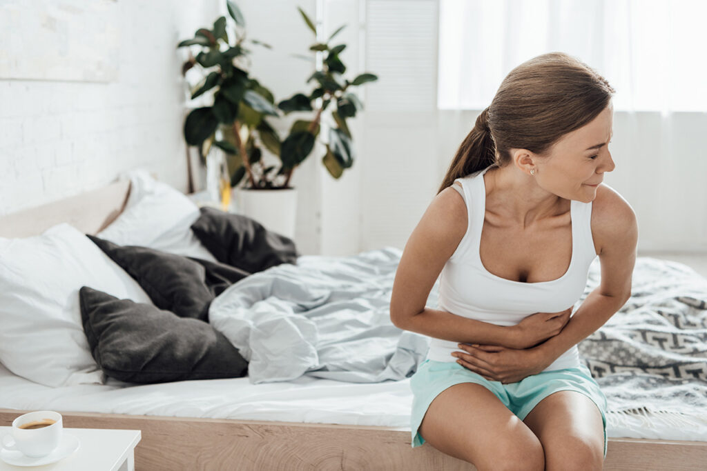 woman sitting on bed with abdominal pain